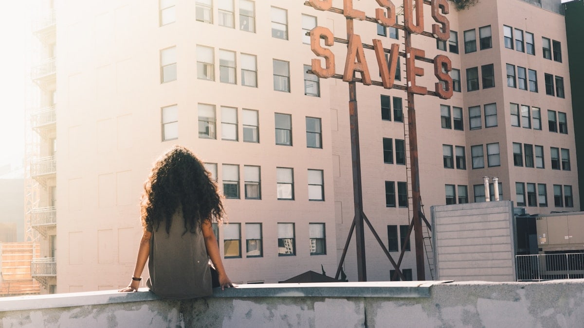 woman in gray top sitting on a building's edge